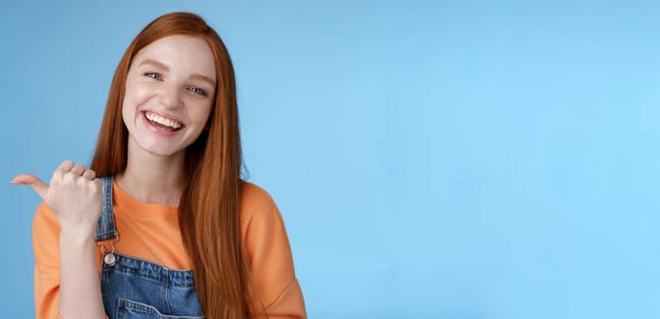 Lifestyle. Girl introducing her friend pointing thumb left smiling laughing joyfully proudly telling pros cool product recommend telling about cozy cafe tasty coffee having fun posing blue background.