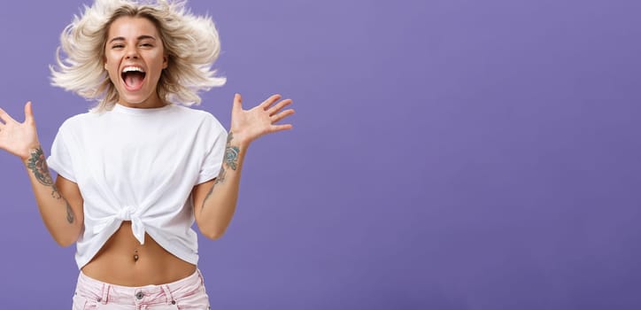 Lifestyle. Studio shot of happy carefree and pleased joyful woman with blonde hair spreading palms aside in delighted pose smiling broadly and gazing entertained at camera jumping while having fun.