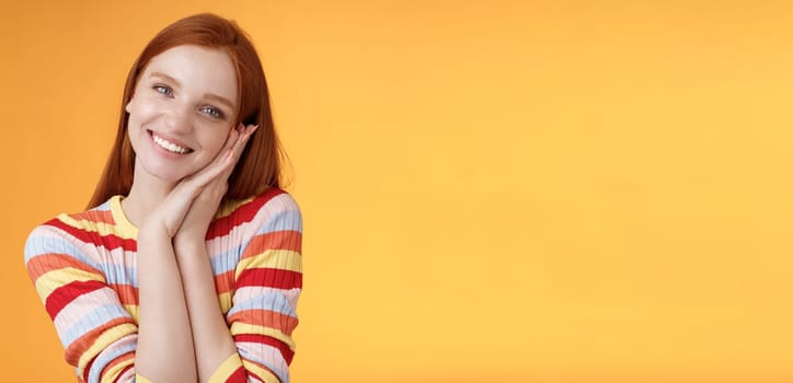 Lovely young flirty redhead european girl smiling broadly excited happy lean palm receive sweet tender present look grateful amused joyfully reacting pleasing moment, standing orange background.