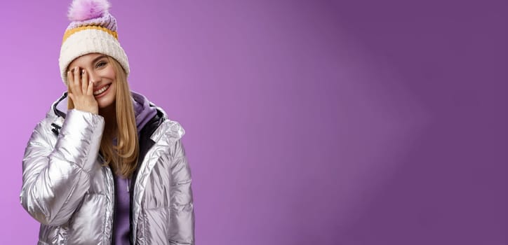 Carefree happy upbeat charming blond woman cover half face tilting head laughing joyfully wearing outdoor stylish silver jacket winter hat having fun awesome five star ski resort, purple background.