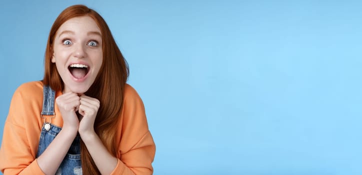 Lifestyle. Cute redhead european girl blue eyes freckles reacting amused shocking rumor lift eyebrows drop jaw surprised smiling excited picked get role theatre play rejoicing astonished blue background.