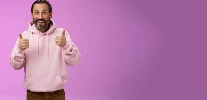 Energized supportive happy charming hipster mature guy bearded grey hair show thumbs up gesture yes approval sign totally agree cheering root for friend like awesome idea, standing purple background.