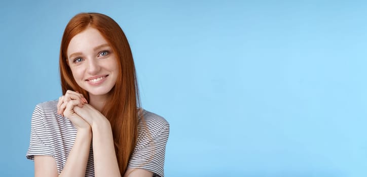 Tender romantic sincere young redhead teenage girl found love look sympathy delight press palms together cute pose smiling happily gazing camera passion lovely grin, blue background.