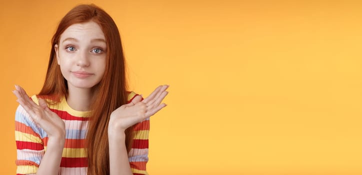 Clueless unbothered young redhead silly european girl 20s shrugging hands spread sideways smirking sorry cannot answer standing unaware confused puzzled give reply, orange background.