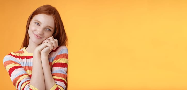Sweet silly tender redhead young girl leaning palms touched smiling receive charming lovely gift standing thankful look affection sympathy accept dearest romantic gesture, orange background.