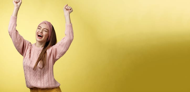 Positive celebating happy european young woman wearing casual sweater yelling happily shouting yes, triumphing racing hands up in success jumping ecstatic rejoicing cheerfully over success. Copy space