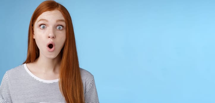 Wow omg fascinating. Impressed surprised amused good-looking redhead girl folding lips astonished wide eyes stunned reacting incredible cool promo standing blue background speechless.