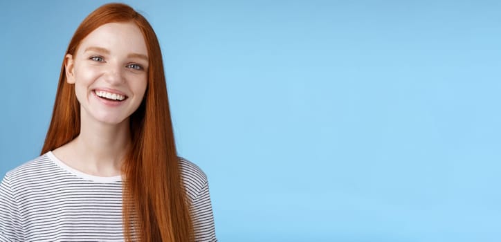 Happy friendly charismatic joyful young sincere 20s redhead girl having fun smiling cheerful laughing joking talking casually grinning camera express positive lucky attitude, standing blue background.