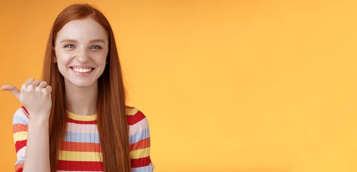 Girl pointing left cool person can help smiling delighted look friendly camera discuss interesting project introduce friend during conversation standing happy grinning orange background.