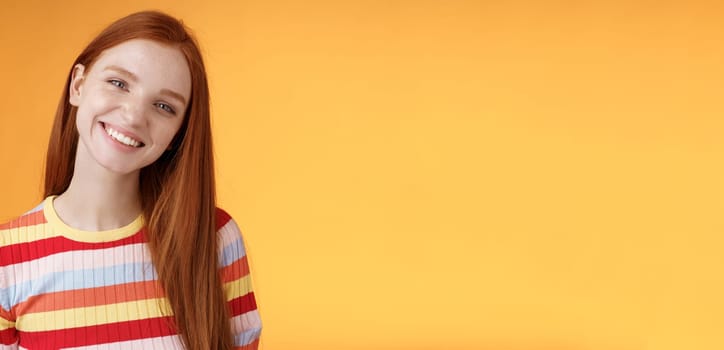 Pleasant charismatic young confident carefree redhead charming girl tilting head smiling broadly white teeth talking casually good mood express positive happy emotions standing orange background.