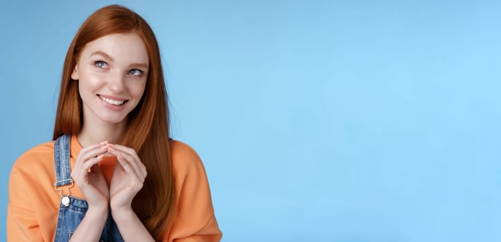 Devious tricky smart pretty redhead girlfriend have evil plan smirking mysteriously look upper left corner twiddles fingers think excellent plan, smiling delighted, standing blue background.