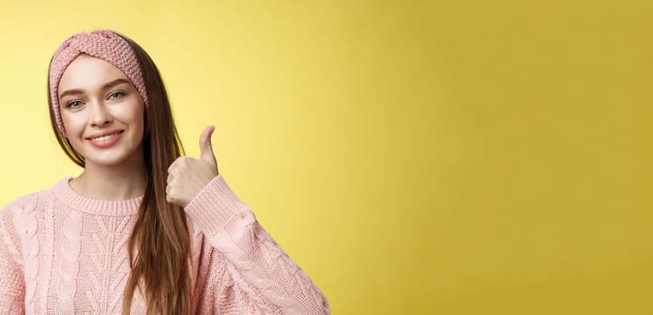 Pretty european young girl in headband, pink sweater smiling delighted, pleased showing thumbs up in agreement, approval, giving good recommendation, liking interesting great idea smiling cheerful.