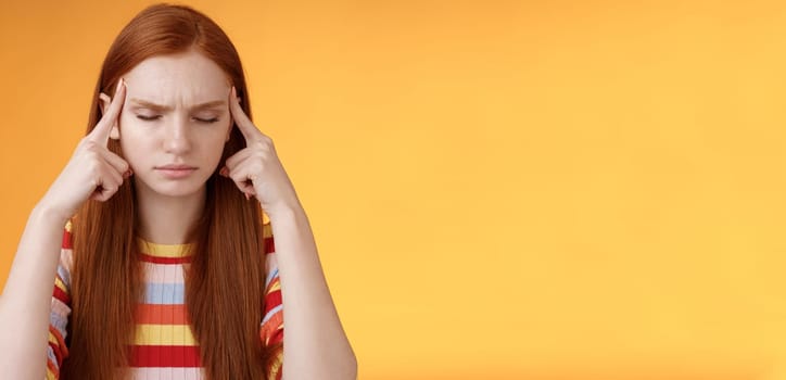 Girl getting thoughts piled trying think stright focusing concentrating important task remember number touch temples close eyes look seriously standing puzzled suffer headache, orange background.