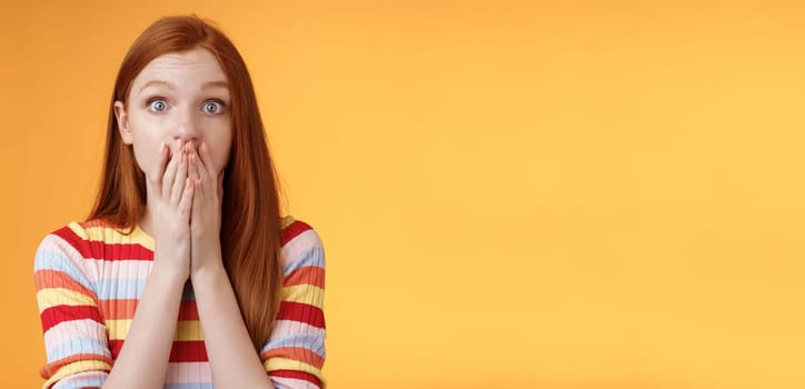 Shocked speechless impressed sensitive redhead european girl reacting stunning rumor gossiping find out secret gasping cover mouth palm stare camera astonished surprised, orange background.
