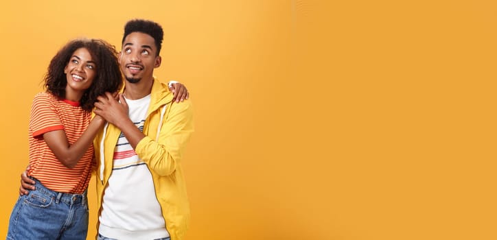 Couple of lovers enjoying spending warm summer evening together gazing up at stars with happy. enthusiastic expression being in love hugging and expressing warm romantic feelings over orange wall.