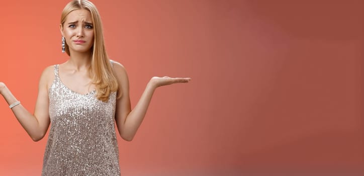 Nervous unsure doubtful cute blond woman struggle make decision shrugging pointing sideways frowning upset standing insecure feel pressure cannot decide choice make, frustrated red background.