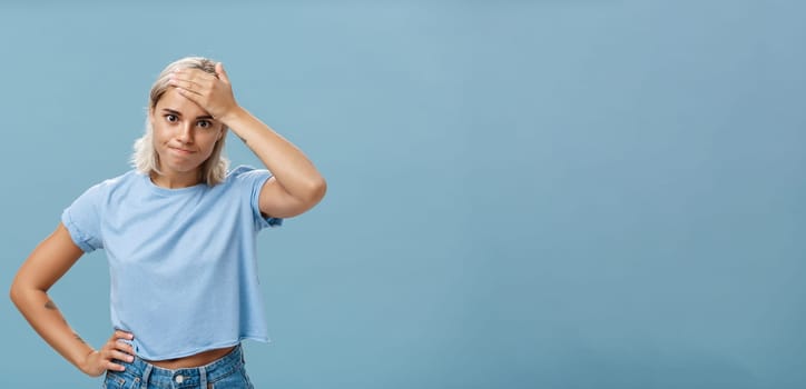 Lifestyle. Girl cannot deal with naughty kids being left alone while mom on shopping holding hand on forehead breathing out losing temper being in troublesome perplexed situation tired over blue background.