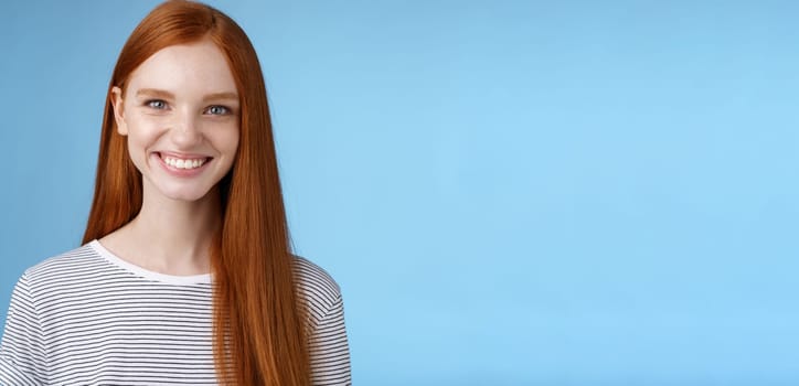 Pleasant reliable sincere good-looking redhead female freelancer college student make confident professional impression smiling broadly assertive helpful standing blue background self-assured.