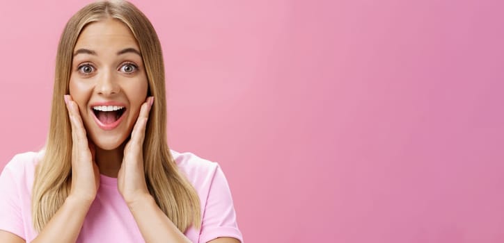 Woman surprised to see own face without imperfactions treating acne feeling beautiful and happy touching cheeks, smiling amazed, joyful looking with admiration and excitement at camera over pink wall.