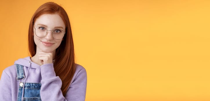 Confident happy relaxed european redhead skillful young female entrepreneur glasses establish startup smiling delighted look pleased result touch chin thoughtful smart, orange background.
