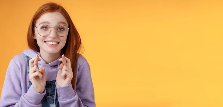 Hopeful young cute silly dreamy redhead attractive girl ginger straight haircut wearing glasses begging lord help cross fingers good luck desire win dream come true praying wish fulfill. Lifestyle.