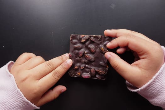 child girl hand pick dark chocolate against gray background ,
