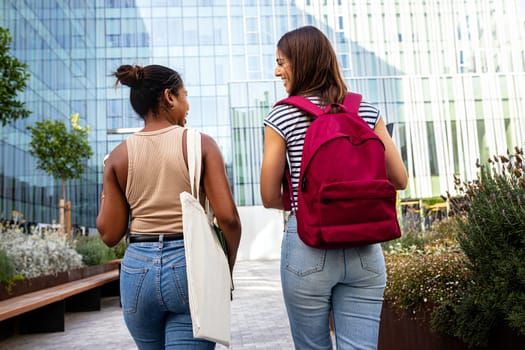 Back view of two multiracial female college students friends walking to class talking and laughing. Education concept.