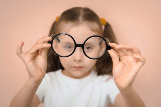 Portrait of an out-of-focus smart preschool girl holding round diopter glasses in front of her in focus.