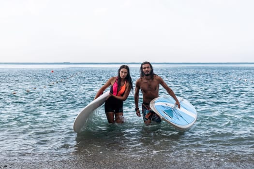 Sea woman and man on sup. Silhouette of happy young woman and man, surfing on SUP board, confident paddling through water surface. Idyllic sunset. Active lifestyle at sea or river