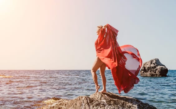 Woman travel sea. Young Happy woman in a long red dress posing on a beach near the sea on background of volcanic rocks, like in Iceland, sharing travel adventure journey