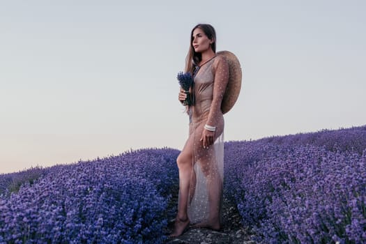 Close up portrait of young beautiful woman in a white dress and a hat is walking in the lavender field and smelling lavender bouquet.