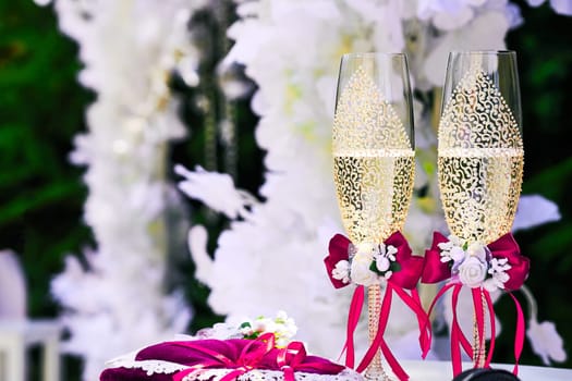 a marriage ceremony, especially considered as including the associated celebrations. Gold wedding crystal glasses of champagne with red ribbons and wedding decor