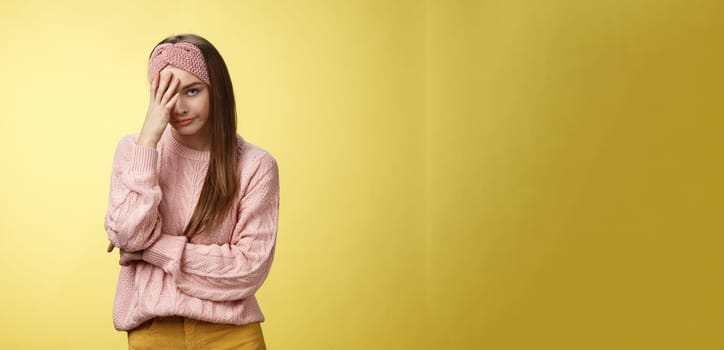 Woman facepalming covering face annoyed, bothered and inrritated, smirking looking with dismay, pissed off, posing unhappy displeased, staring indignant and upset posing tired over yellow background.