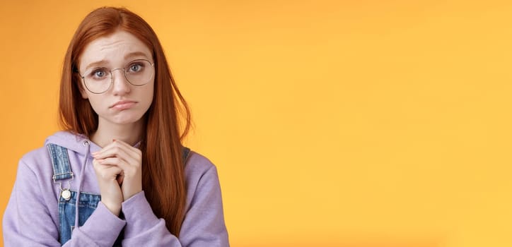 Pretty please. Clingy young sad sulking redhead girl sibling wearing glasses pouting silly press palms begging gesture pleading wanna receive help promise be good ask favour, orange background.