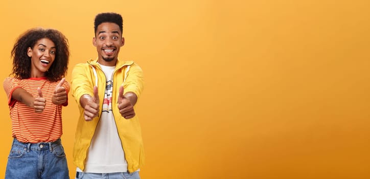 Two friends like perfect and awesome plan. Portrait of joyful friendly-looking optimistic african american female and male showing thumbs up in approval and agreement gesture smiling broadly. Copy space