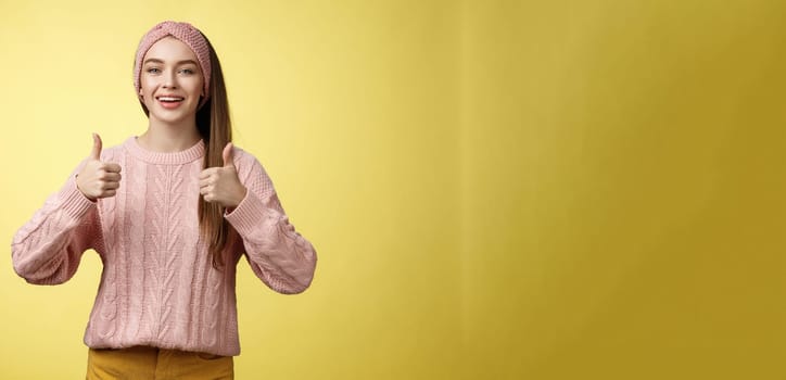 Attractive positive young girl in knitted sweater agree with suggestion, approving plan, showing thumbs up, recommending awesome film, smiling, cheering, supporting friend effort, encouraging.