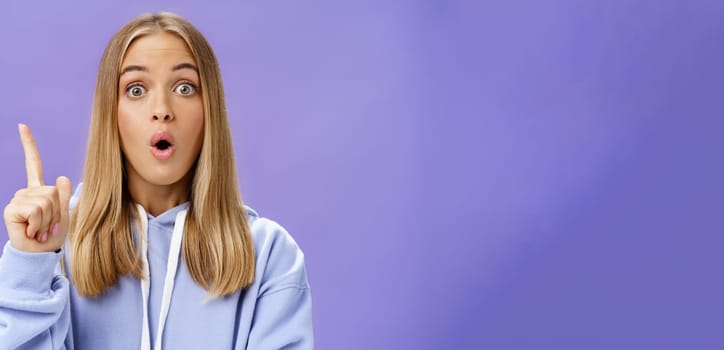 Oh I know idea. Excited cute young woman with tan in hoodie raising index finger in eureka gesture folding opened lips and staring amazed at camera having suggestion what do over blue background. Copy space