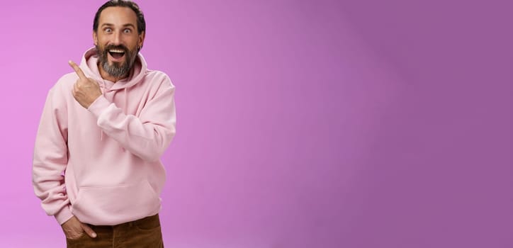 Speechless excited impressed handsome bearded man grey hair widen eyes surprised astonished wow drop jaw gasping thrilled pointing upper left corner see famous star, purple background.