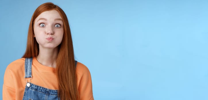 Lifestyle. Cute childish playful charming redhead girl popping blue eyes staring camera hold breath inhale air mouth standing speechless promise not slip secret acting immature standing funny happily.