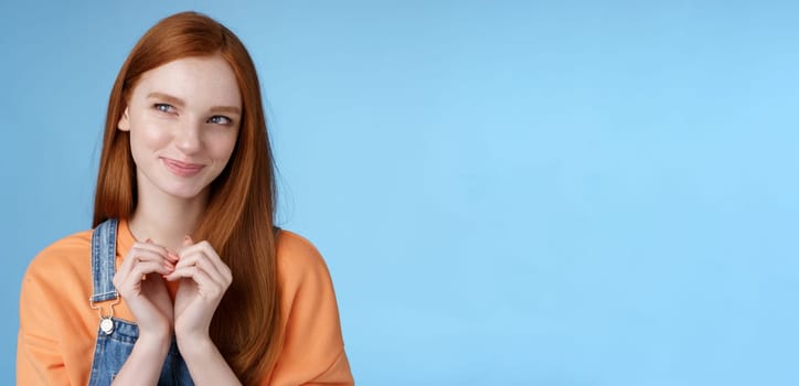 Devious tricky young girl have excellent plan smirking delighted mysteriously look upper left corner smiling have idea thoughtfully twiddles fingers standing rejoicing blue background.