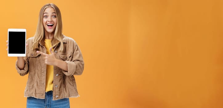 Woman showing friends new digital tablet first purchace of autumn. Charismatic and enthusiastic excited caucasian female with tanned skin and fair hair in corduroy jacket pointing at gadget screen. Emotions and technology concept