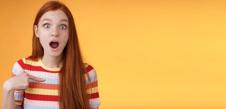 Lifestyle. Shocked silly surprised redhead cute girl gasping drop jaw stunned stare camera full disbelief pointing herself cannot believe chosen picked participate event standing impressed orange background.