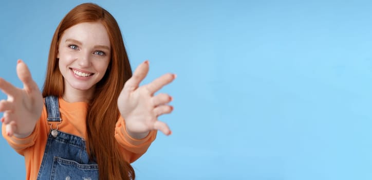 Come into arms. Charming sincere happy kind redhead girl baby sitting stretch hands camera wanna hold catch smiling friendly asking pass object, standing blue background reach friend give cuddles.