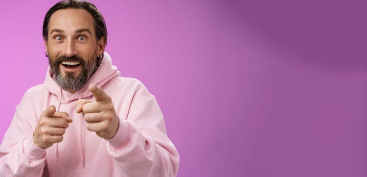 Thrilled energized charismatic happy lucky adult handsome bearded man pointing camera smiling widen eyes gazing impressed see famous person express amazement joy, purple background.