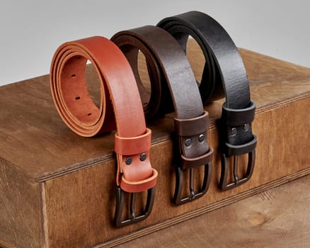 Collection of three rolled leather belts of different colors with metal buckles and DAD embossing on loops, displayed on wooden podium steps