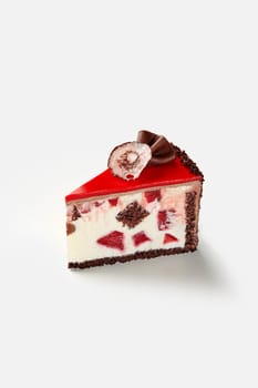 Slice of luxurious chocolate sponge cake layered with whipped cream and sour cream, complemented by berry jelly and dessert cherries and topped with chocolate ganache and red icing, isolated on white