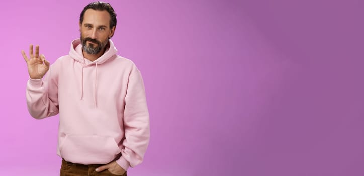 Confident good-looking lucky old macho guy bearded grey hair in stylish pink hoodie hold hand pocket show okay ok approval gesture smirking delighted agree daughter choice, posing supportive.