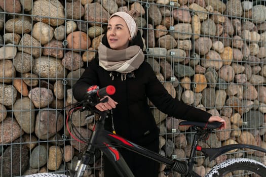 European cute woman headband wearing a black long coat rides a bicycle.