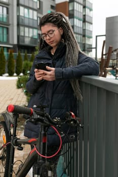 A pretty young woman with a dreadlocked hairstyle rides a bicycle and stops to rest.
