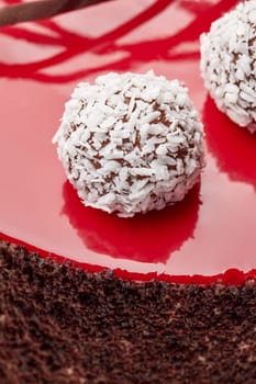 Closeup of chocolate truffles covered with coconut flakes arranged on red glossy glaze decorating delicious tempting cake. Traditions of confectionery art